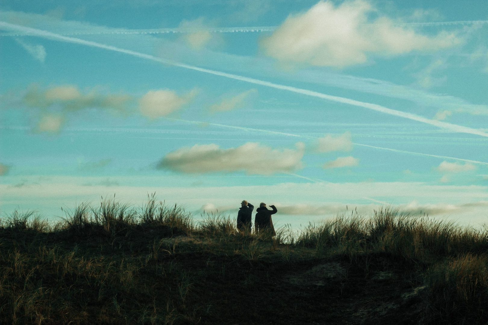 Two people searching for something against a cloudy blue sky